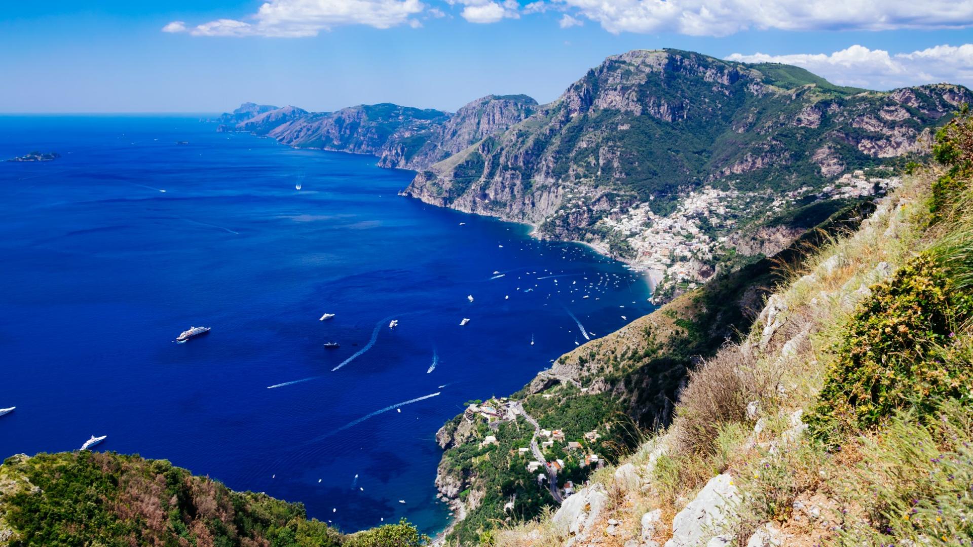 Vista panoramica della Costiera Amalfitana con mare blu e montagne verdi.