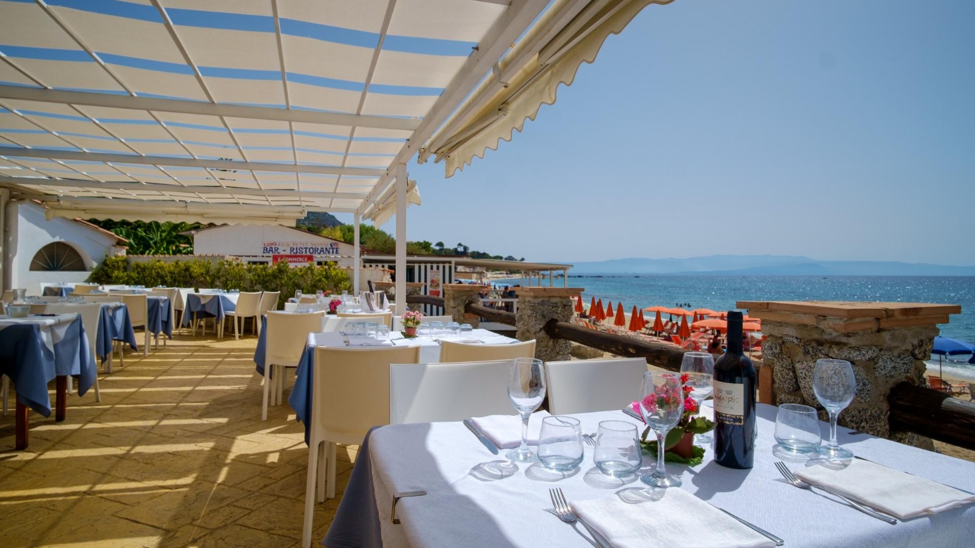 Ristorante all'aperto sul mare con tavoli apparecchiati e vista sulla spiaggia.