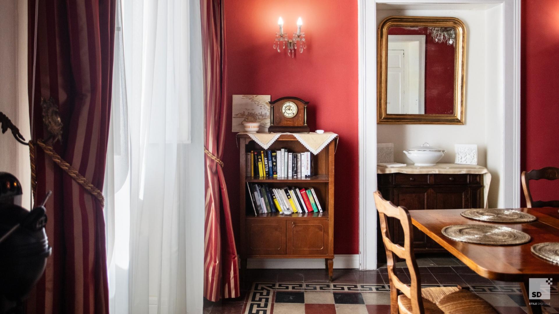 Sala da pranzo elegante con pareti rosse, libreria e specchio dorato.