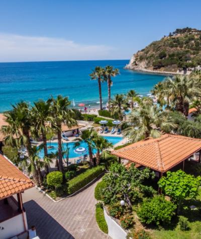 Vista su spiaggia, mare azzurro, palme e strutture turistiche con tetti rossi.