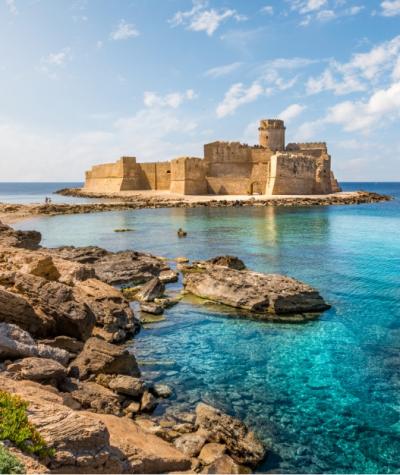 Castello sul mare con acque cristalline e cielo sereno, paesaggio mozzafiato.