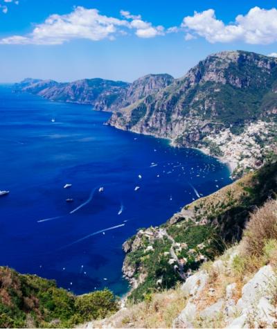 Vista panoramica della Costiera Amalfitana con mare blu e montagne verdi.