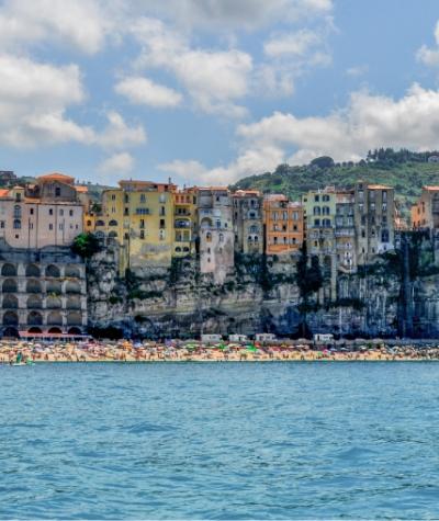 Case colorate sulla scogliera, affacciate su una spiaggia affollata e mare blu.