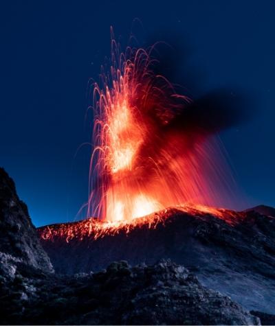 Eruzione vulcanica notturna con lava incandescente e cielo stellato.