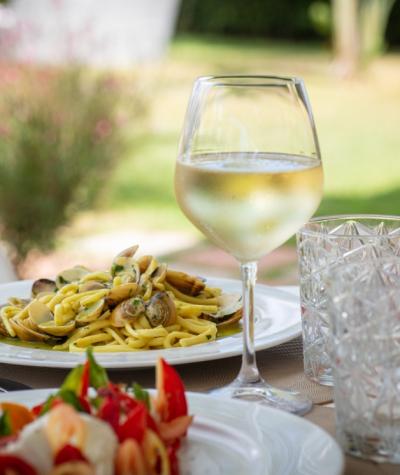 Piatto di pasta con vongole e bicchiere di vino bianco in giardino.