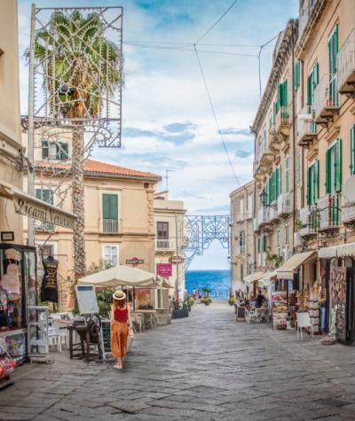 Strada pittoresca con negozi, vista sul mare e decorazioni luminose.