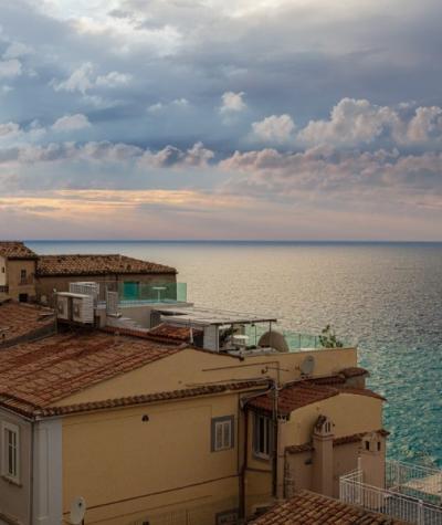 Vista sul mare con case dai tetti rossi e cielo nuvoloso.