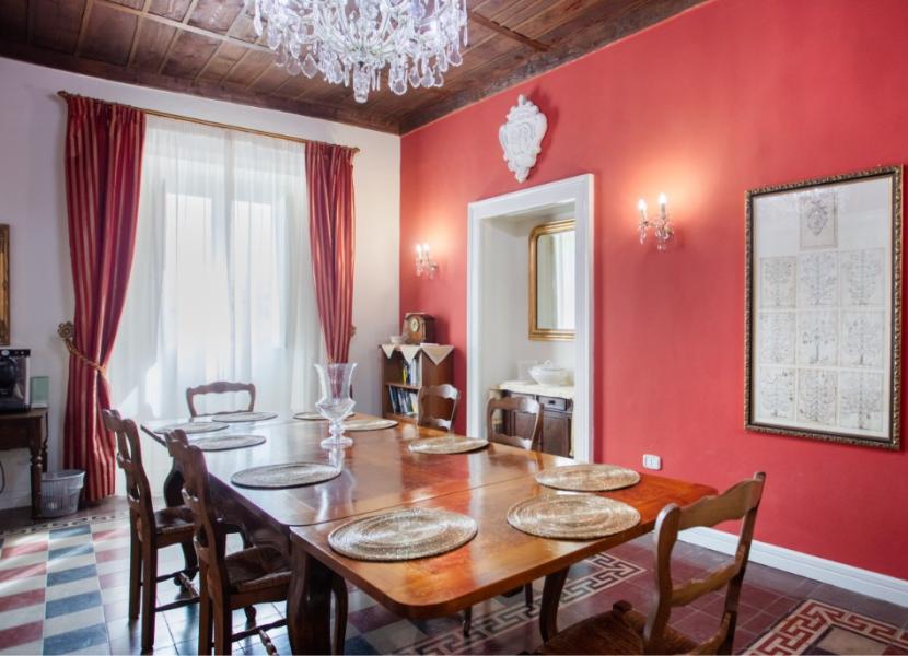 Sala da pranzo elegante con pareti rosse, tavolo in legno e lampadario a cristalli.