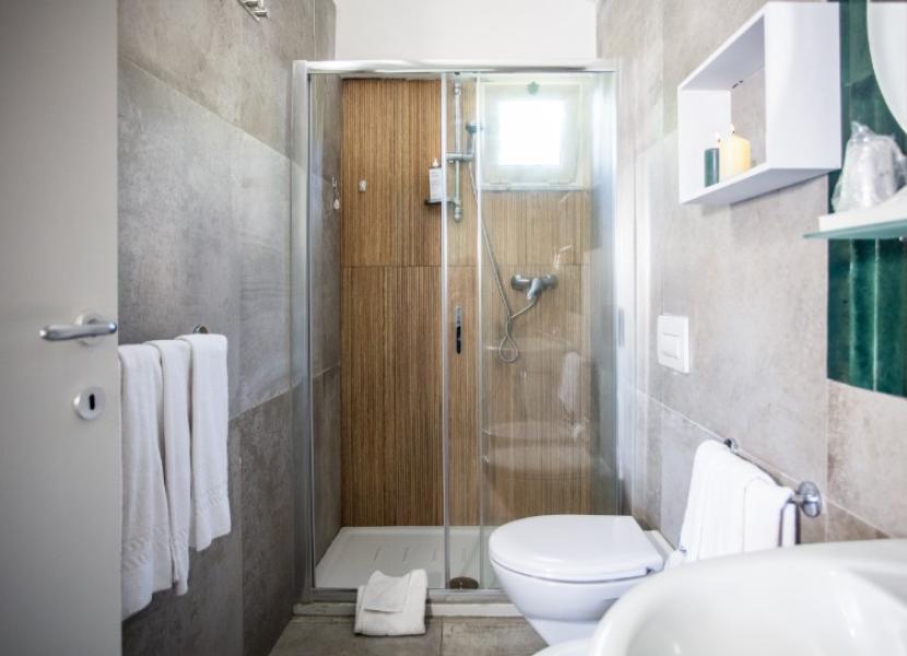 Bagno moderno con doccia, WC e asciugamani bianchi, arredamento minimalista e luminoso.