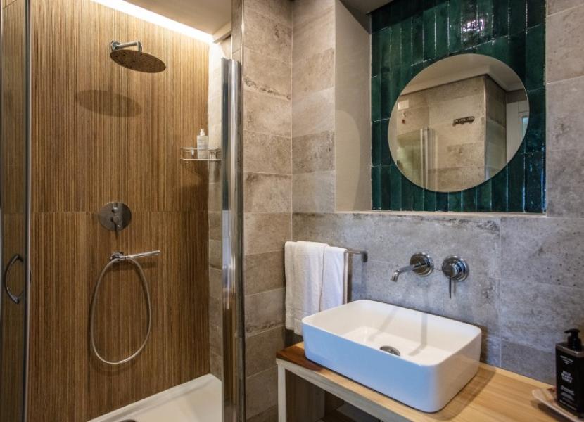 Bagno moderno con doccia, lavabo rettangolare, specchio rotondo e piastrelle verdi.