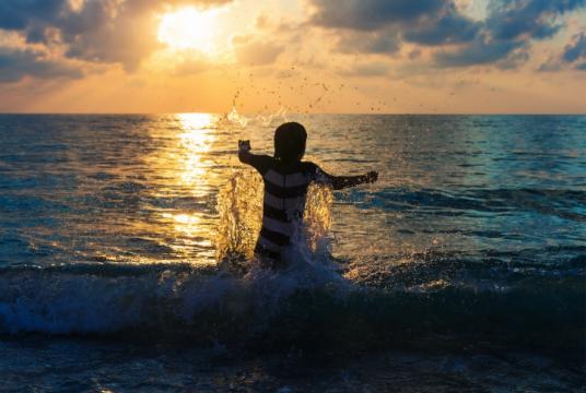 Persona in acqua al tramonto, spruzzi e onde sotto un cielo nuvoloso.